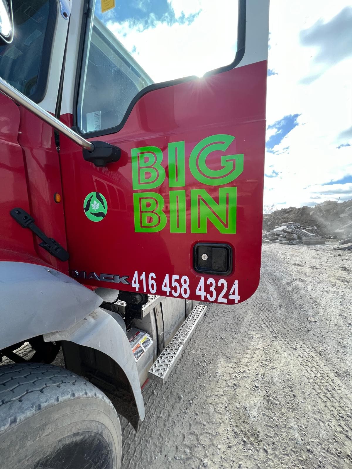 Close-up of a Big Bin truck door showing the logo and phone number, with broken concrete behind it